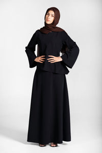 Woman wearing a modest black skirt and top set with a brown hijab on a white background
