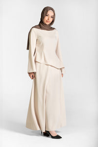 Woman wearing a beige/cream top and skirt coord set with a brown hijab on a white background