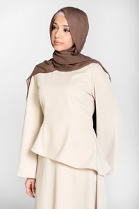Woman wearing a beige top and skirt coord set with a brown hijab on a white background