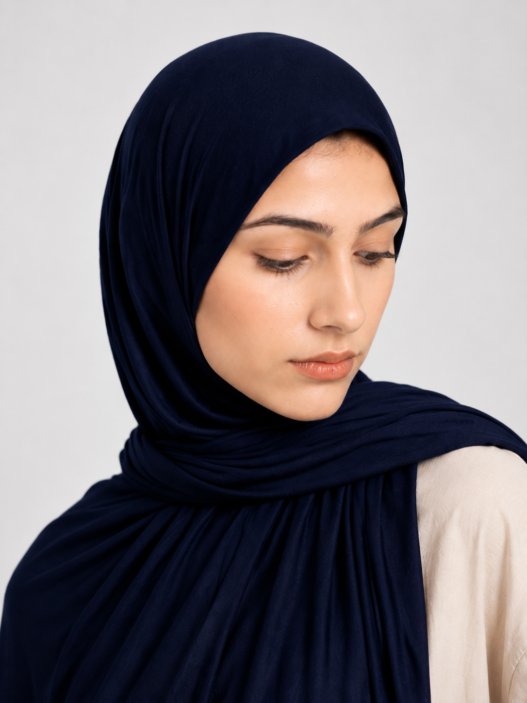 Woman wearing a dark navy blue jersey hijab against a white background