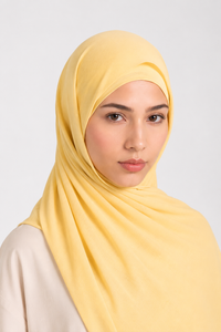 A woman wearing a soft pastel yellow Modal hijab, styled with a light beige top, photographed against a neutral light gray background.